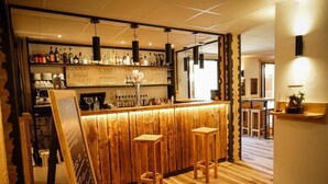A bar area with wooden bar counter, stools, and shelves of bottles and glasses. - Le Faranchin (Villar-d'Arene)