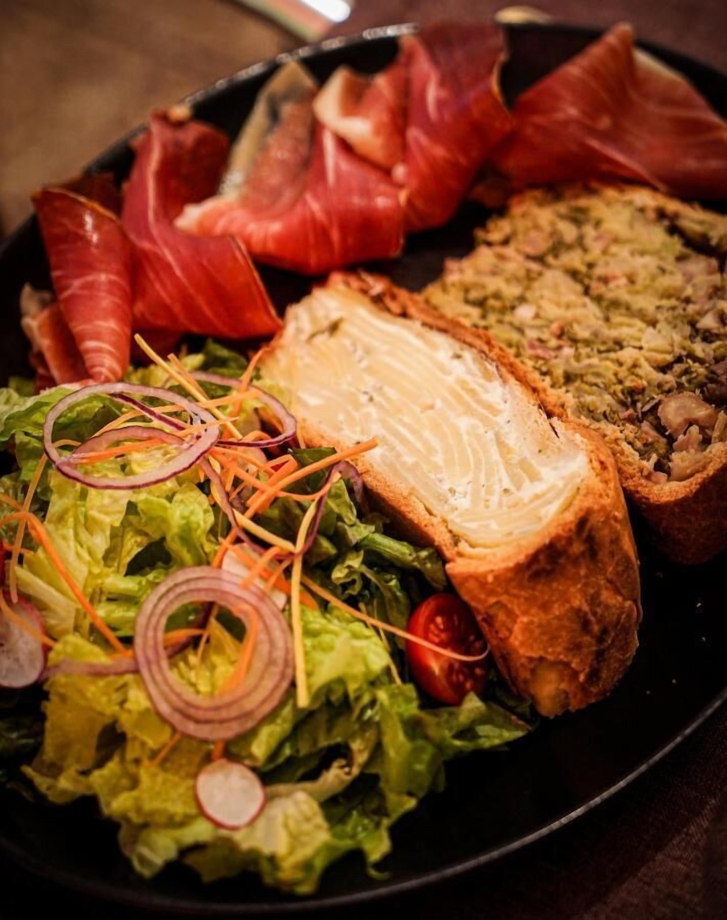 A plate with various food items including a slice of salmon, a salad with lettuce, radishes, and onions, and a piece of bread with a spread.