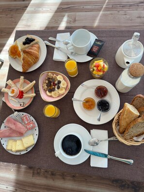 A breakfast spread on a wooden table with croissants, fruit, yogurt, cheese, and coffee. - Le Faranchin (Villar-d'Arene)