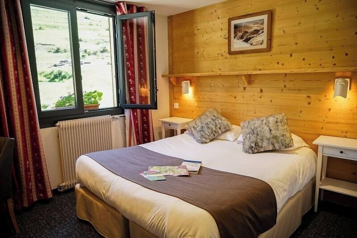 A hotel room with a bed, a window with curtains, a radiator, and a wall-mounted picture.