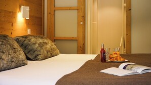 A bed with a blanket, pillows, a plate with croissants, a bottle, and a glass. - Le Faranchin (Villar-d'Arene)