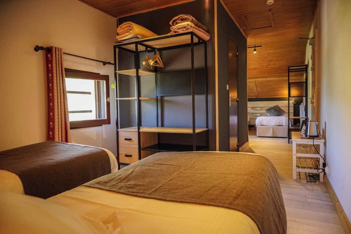A bedroom with two beds, a wardrobe, a desk, and a view of another room.