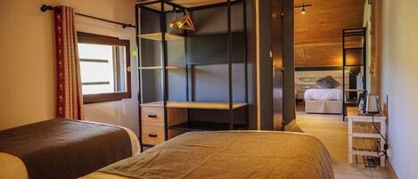 A bedroom with two beds, a wardrobe, a desk, and a view of another room.