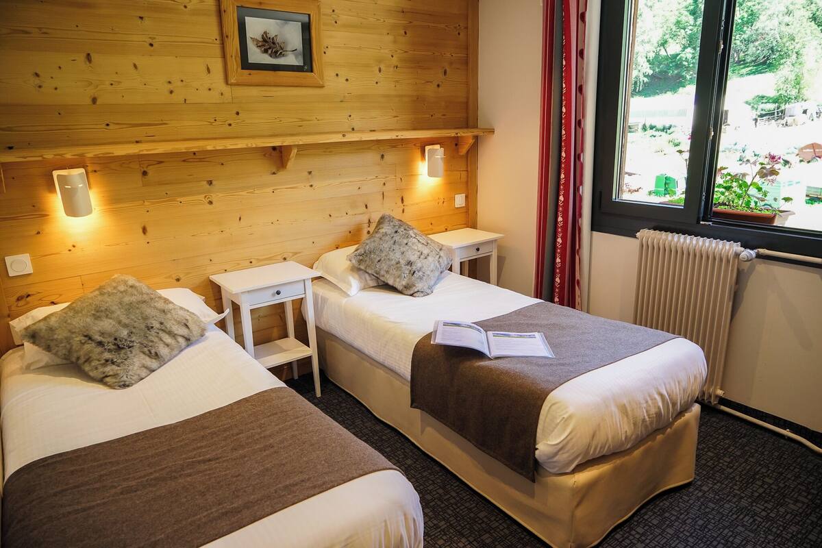 A hotel room with two beds, wooden walls, a window with a view of the outdoors, and a radiator.