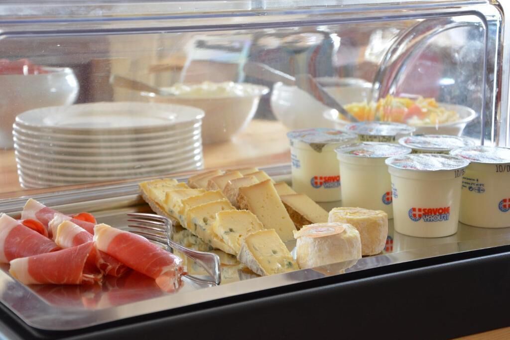 A buffet with various cheeses, meats, and yogurt cups.