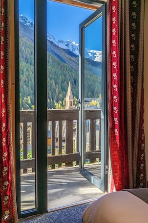A room with a large window, a wooden balcony, and a view of snow-capped mountains.. Le Faranchin