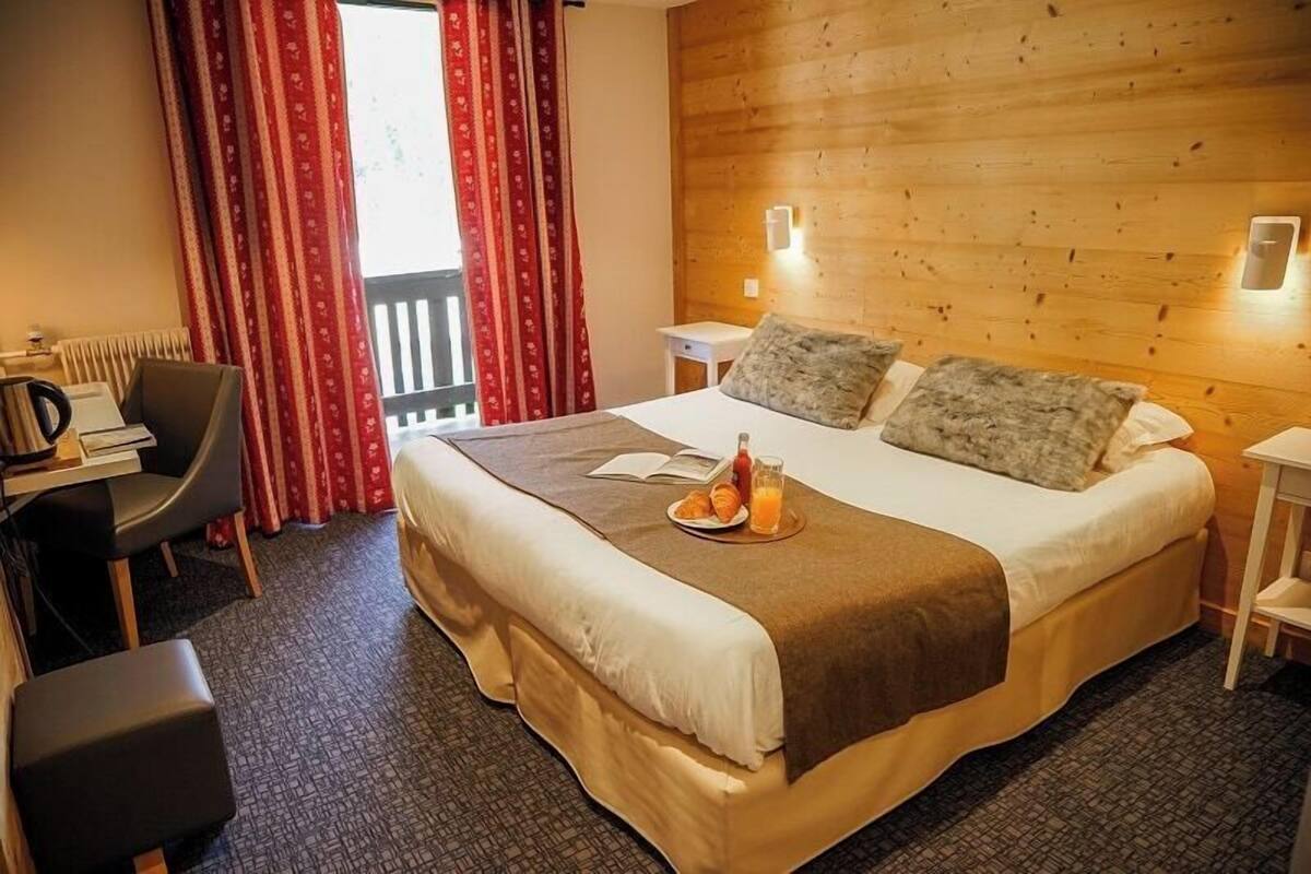 A hotel room with a bed, a desk, a chair, a small table, and a window with curtains.