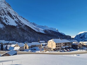 A snow-covered village with traditional buildings, a prominent hotel with a sign, and mountains in the background. - Le Faranchin (Villar-d'Arene)