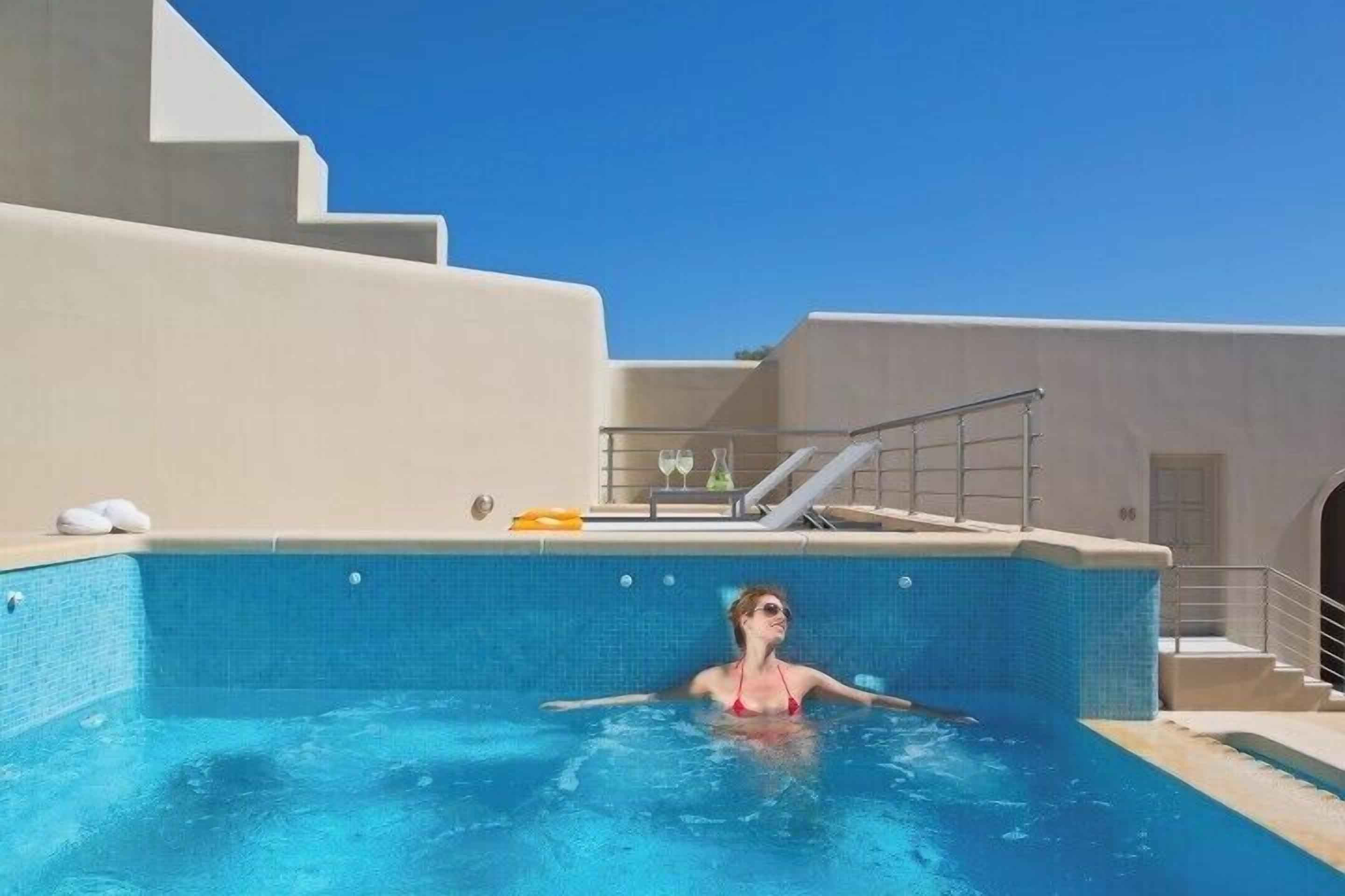 A pool area with a person in a red swimsuit, clear blue water, and a white tiled wall.