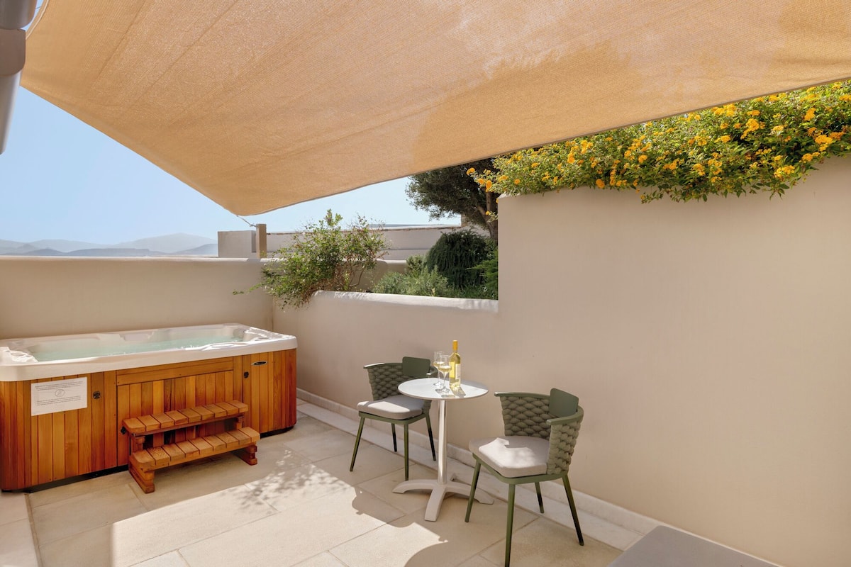 Eine Dachterrasse mit Whirlpool, zwei Stühlen, einem kleinen Tisch und einem Wandkasten mit gelben Blumen.