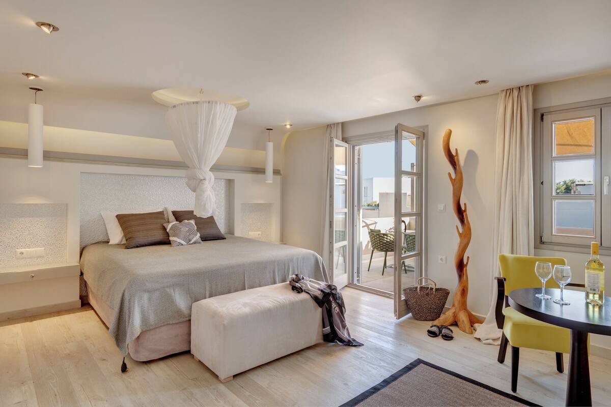 Ein modernes Schlafzimmer mit einem großen Bett, Nachttischen, einer Nachttischlampe, einem Himmelbett, einem Balkon mit Tisch und Stühlen und Meerblick.