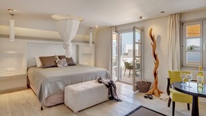 Un dormitorio moderno con una cama grande, mesitas de noche, lámparas de noche, cama con dosel, un balcón con mesa y sillas, y vista al mar.
