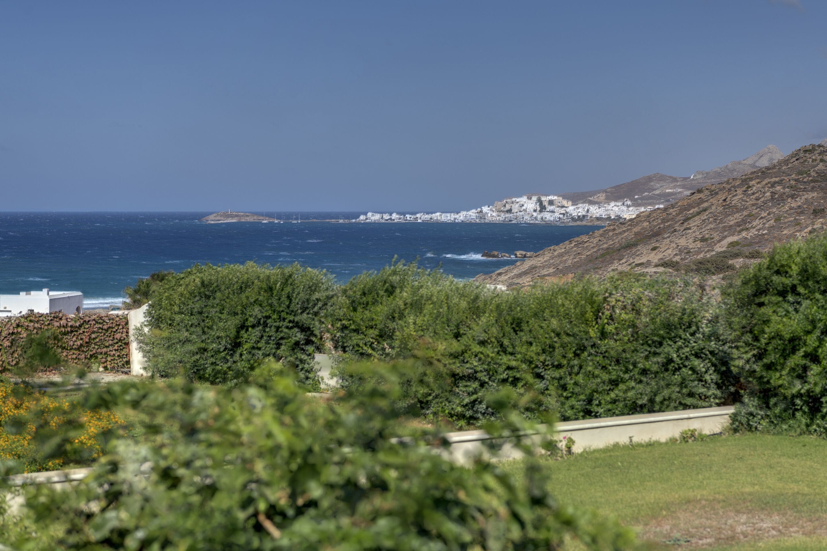 Eine Küstenlandschaft mit Blick auf das Meer, ein Hügel mit Gebäuden und üppigem Grün im Vordergrund.