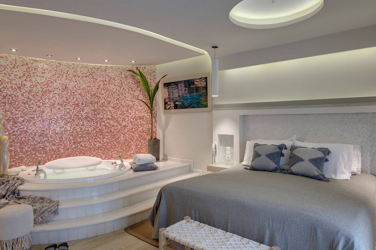 Ein modernes Schlafzimmer mit einem großen Bett, einer Sitzecke mit einer Bank, einer Badewanne und einer Topfpflanze.