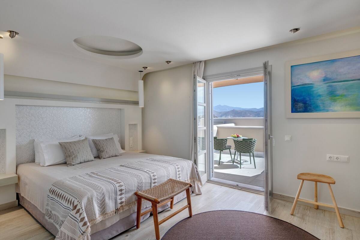 Ein Schlafzimmer mit Bett, einer Bank, einem kleinen Tisch und Blick ins Freie.