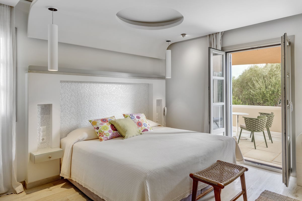 Ein Schlafzimmer mit Bett, Nachttisch, Stuhl und Fenster mit Blick ins Freie.