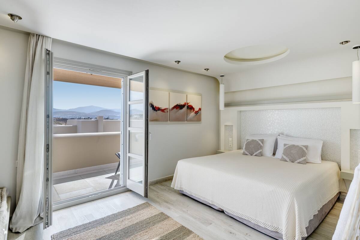 Ein modernes Hotelzimmer mit einem großen Bett, einer Schiebetür zum Balkon und Blick auf die Stadt.