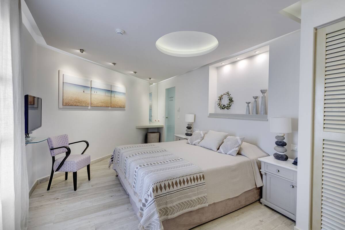 Ein Schlafzimmer mit Bett, einem Sessel, einem Fernseher und einer Wand mit Kunstwerken.