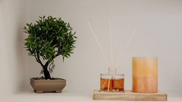 A potted bonsai tree, a glass bottle with reed sticks, and a cylindrical candle on a wooden block.