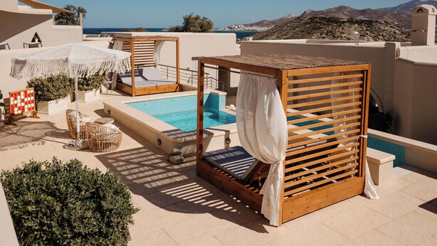 Un área de piscina en la azotea con una cabaña de madera, sillones de descanso y vistas al mar y a las montañas.
