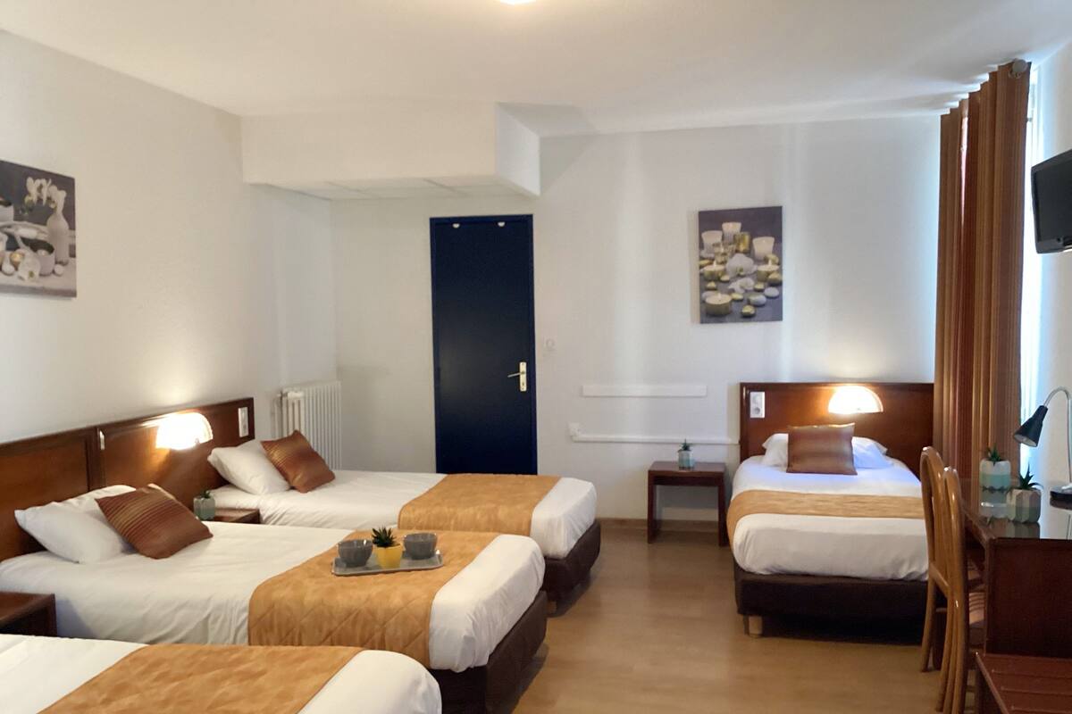Habitación de hotel con tres camas, un escritorio y un televisor.