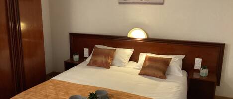 A neatly made bed with a quilted bedspread, two pillows, and a tray with cups and a plant.