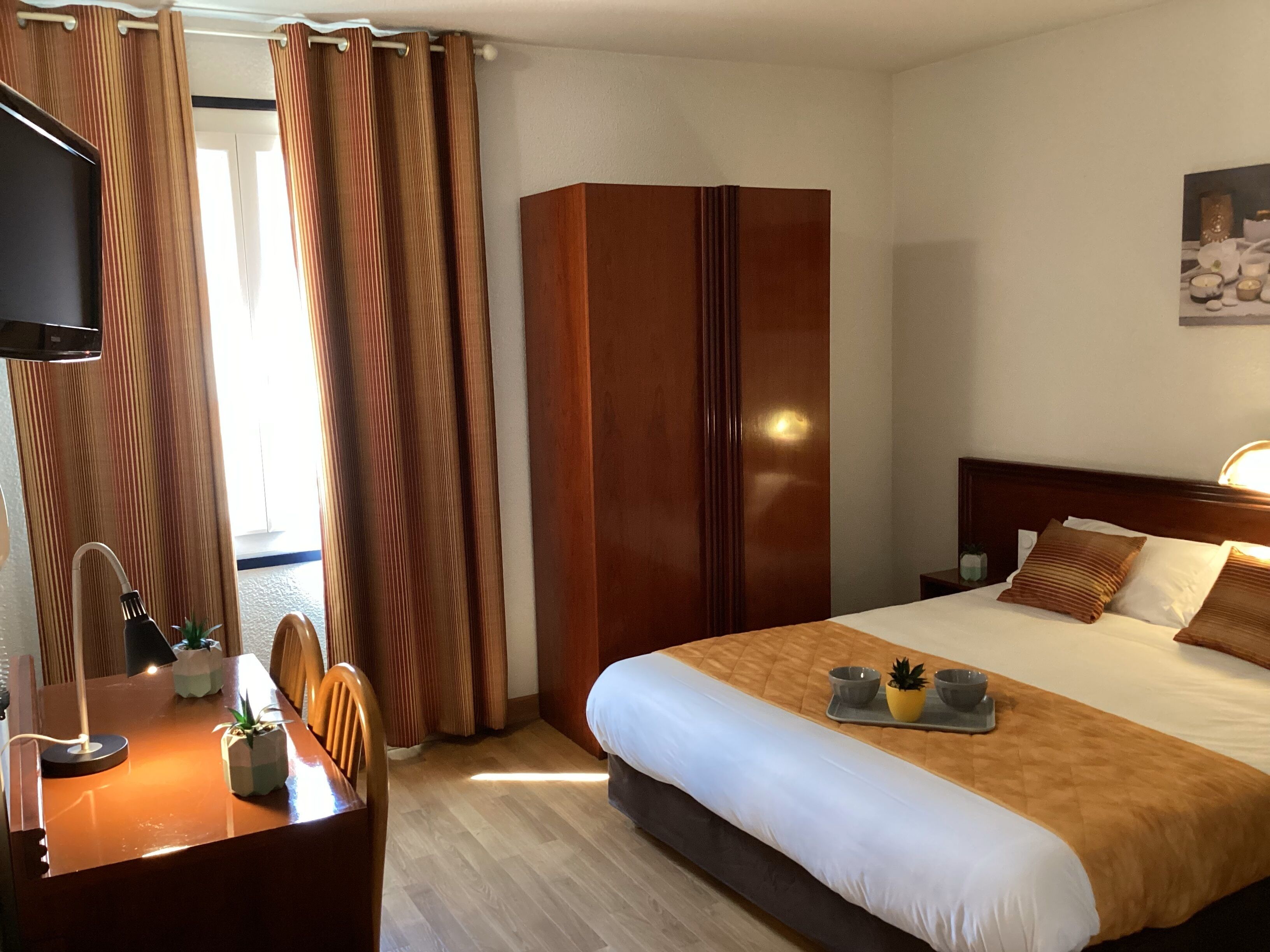 A hotel room with a bed, bedside table, TV, and curtains.