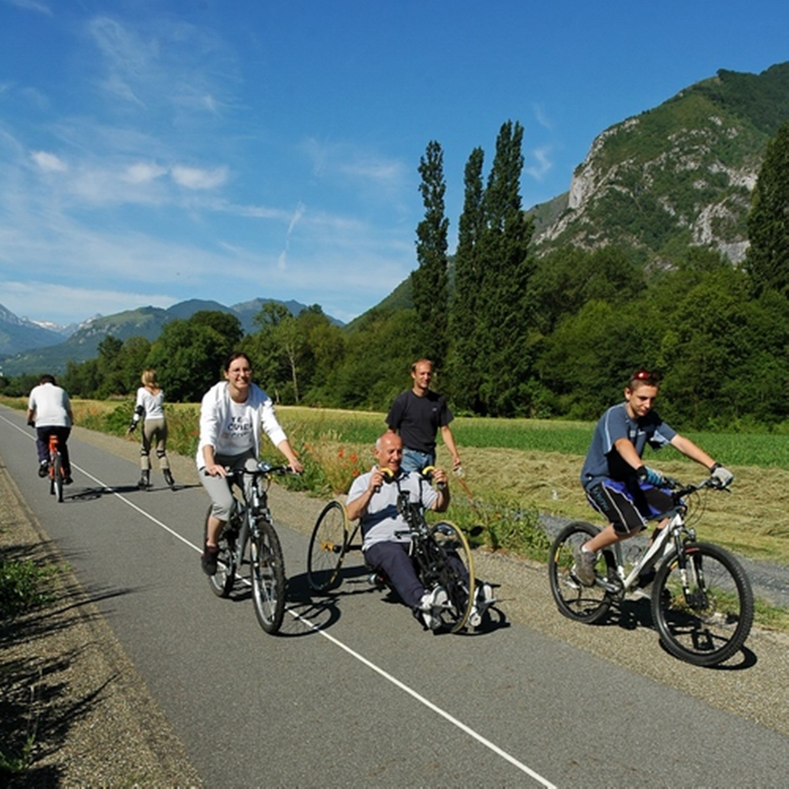 A group of cyclists on a paved path with a mountainous backdrop.