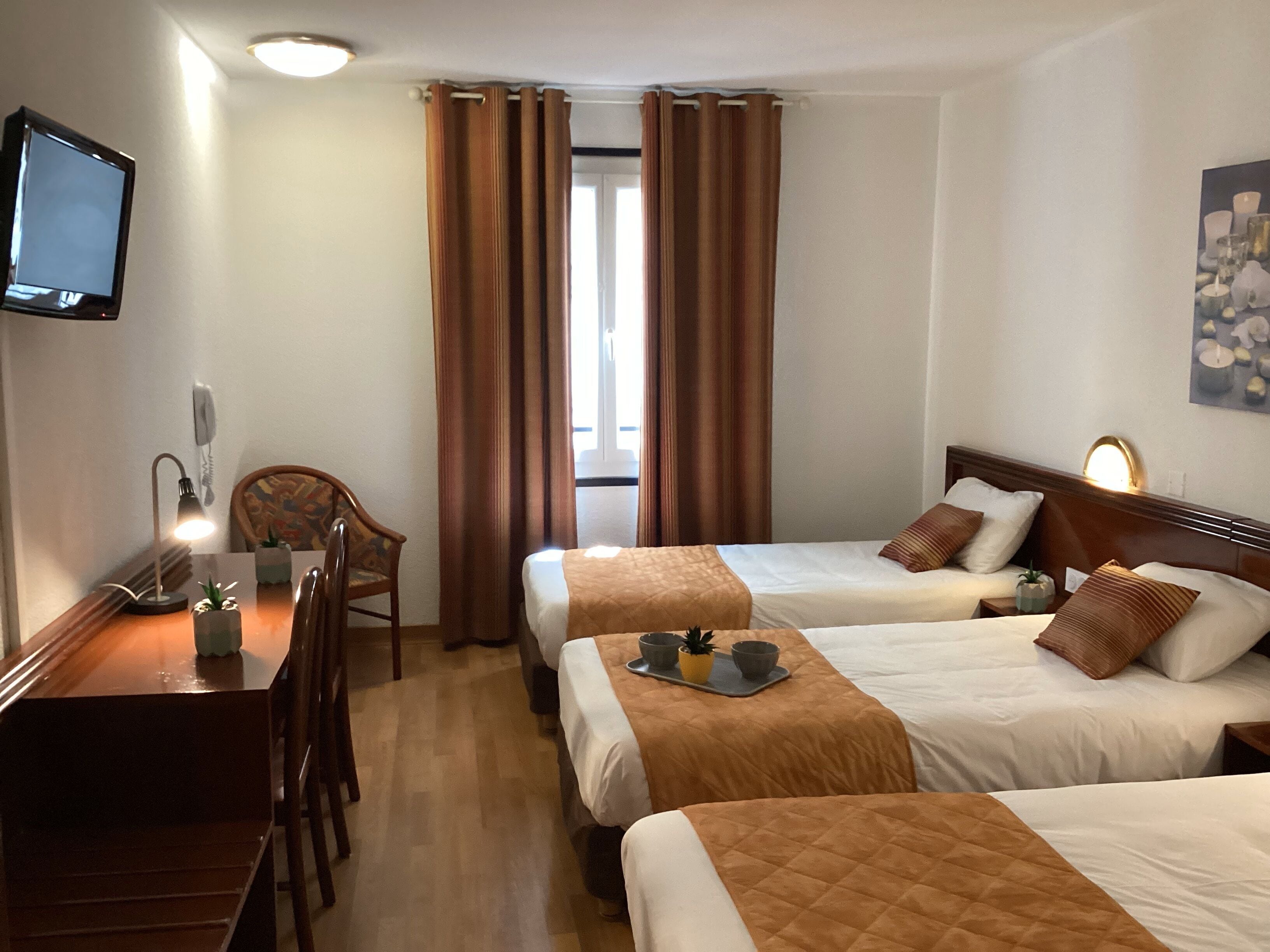 A hotel room with two beds, a desk, a chair, a television, and a window with curtains.