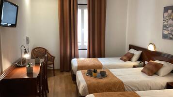 A hotel room with two beds, a desk, a chair, a television, and a window with curtains.