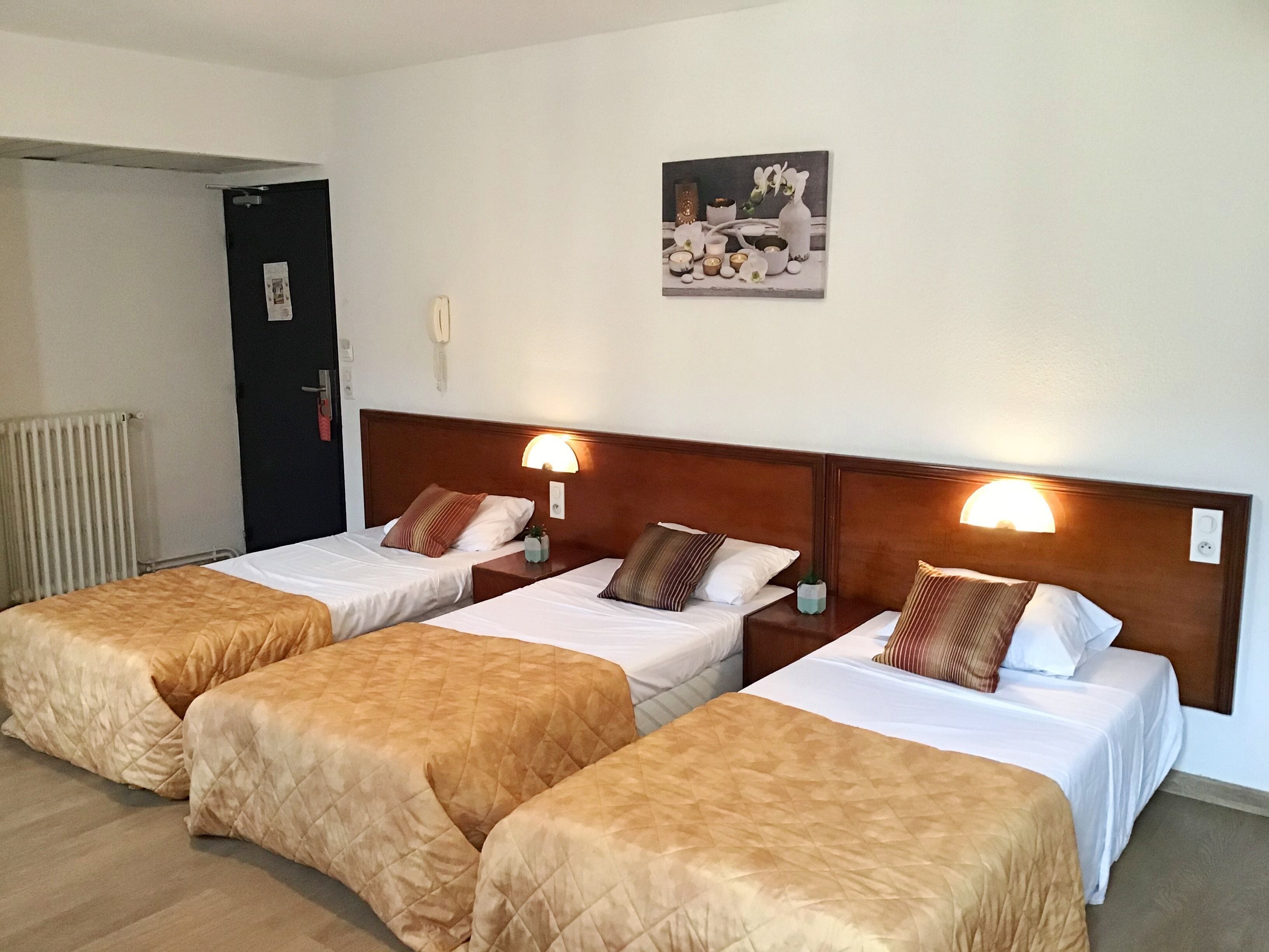 A hotel room with three single beds, each with a wooden headboard and bedside lamps.