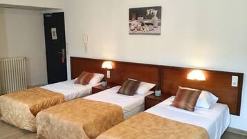 A hotel room with three single beds, each with a wooden headboard and bedside lamps.