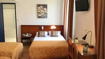 A hotel room with two beds, a bedside table with a lamp, a TV mounted on the wall, and a painting above the bed.