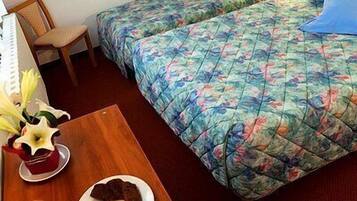 A hotel room with two beds, a wooden table with a plate of food and a glass of orange juice, and a chair.