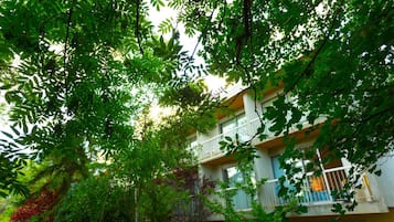 Un immeuble à plusieurs étages doté de balcons, entouré d’une végétation luxuriante.