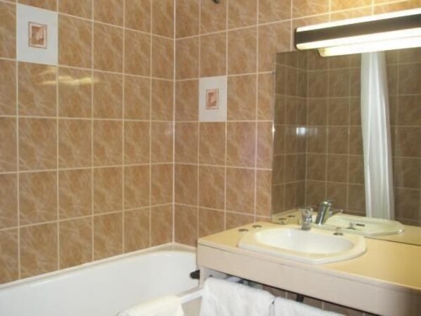 Un baño con baldosas color crema, un lavabo blanco, un espejo y una cortina de ducha.