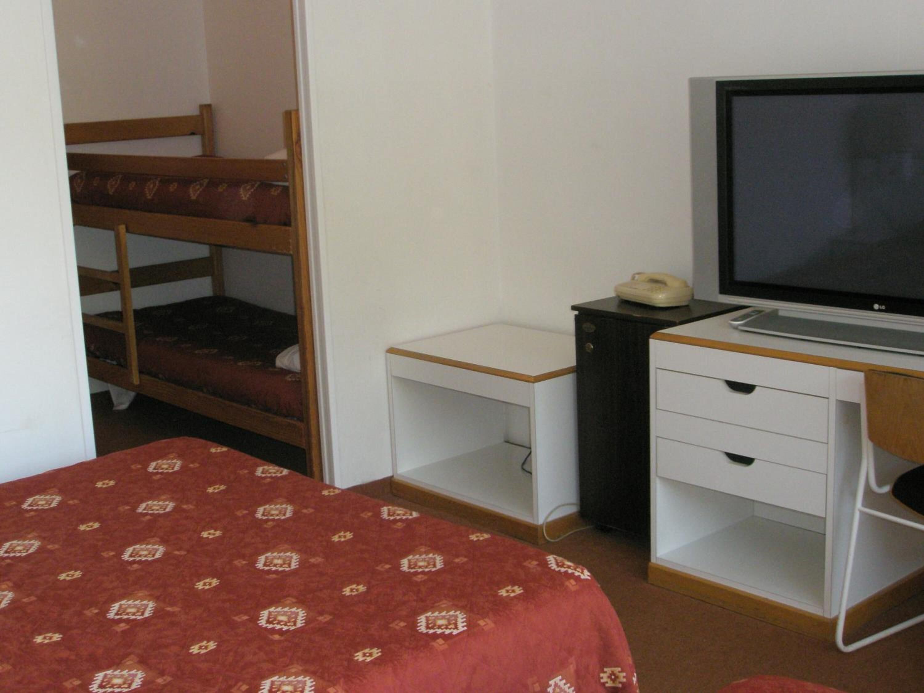 Quarto com beliches, uma escrivaninha com computador, telefone e televisão.