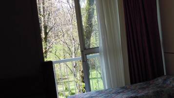 Une chambre avec deux lits, une fenêtre avec des rideaux et une vue sur les arbres et l’herbe.