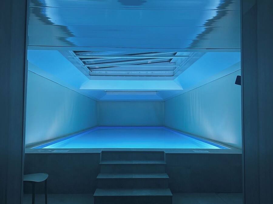 Una habitación con iluminación azul, una escalera que baja a un nivel inferior y una pequeña silla blanca.