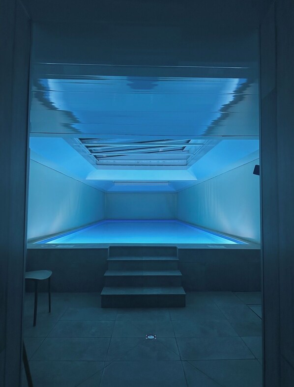 Une pièce dont l’intérieur est éclairé d’une lumière bleue, un escalier menant à un niveau inférieur et une petite chaise blanche.