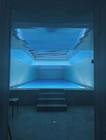 Une pièce dont l’intérieur est éclairé d’une lumière bleue, un escalier menant à un niveau inférieur et une petite chaise blanche.