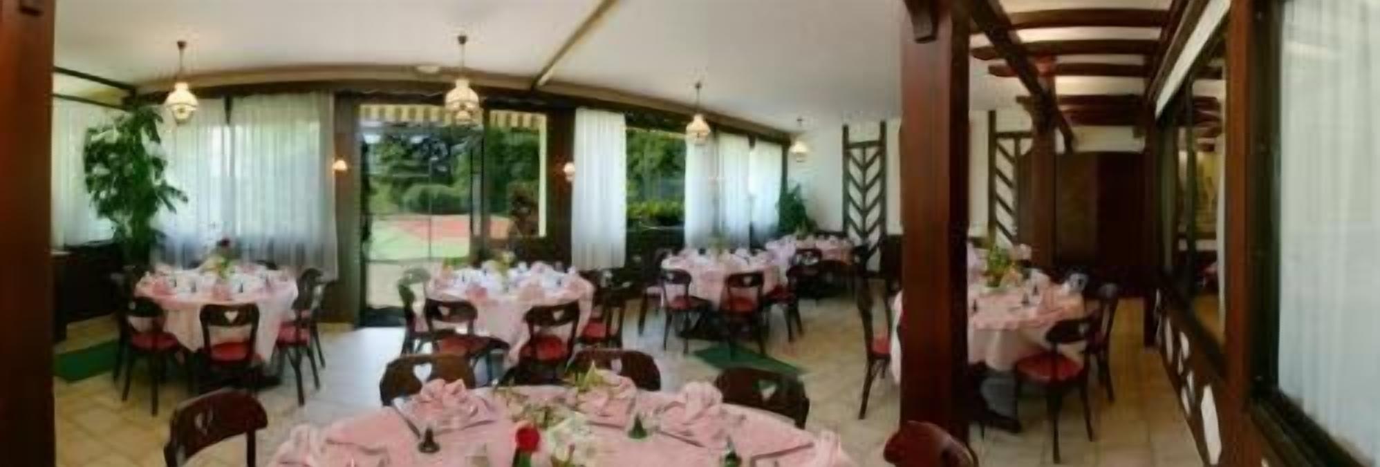 Un espace repas avec des tables rondes disposées pour accueillir plusieurs personnes, chaque table étant recouverte d’une nappe blanche et entourée de chaises rouges.
