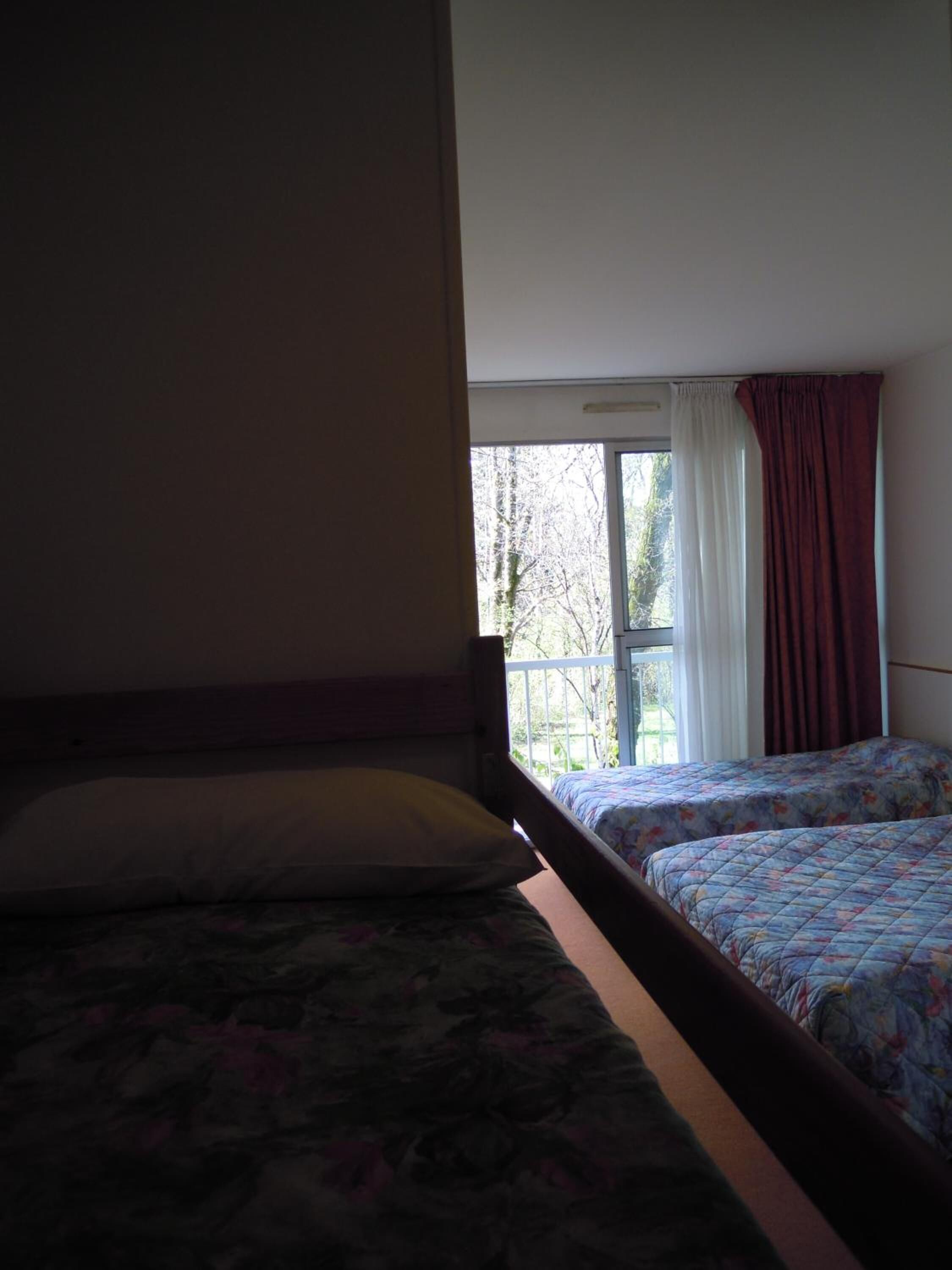 Una habitación con dos camas, una ventana con cortinas y vista a árboles.