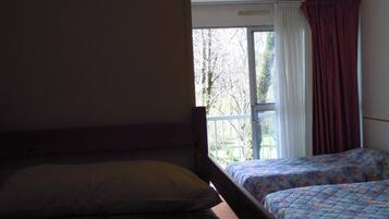 Una habitación con dos camas, una ventana con cortinas y vista a árboles.