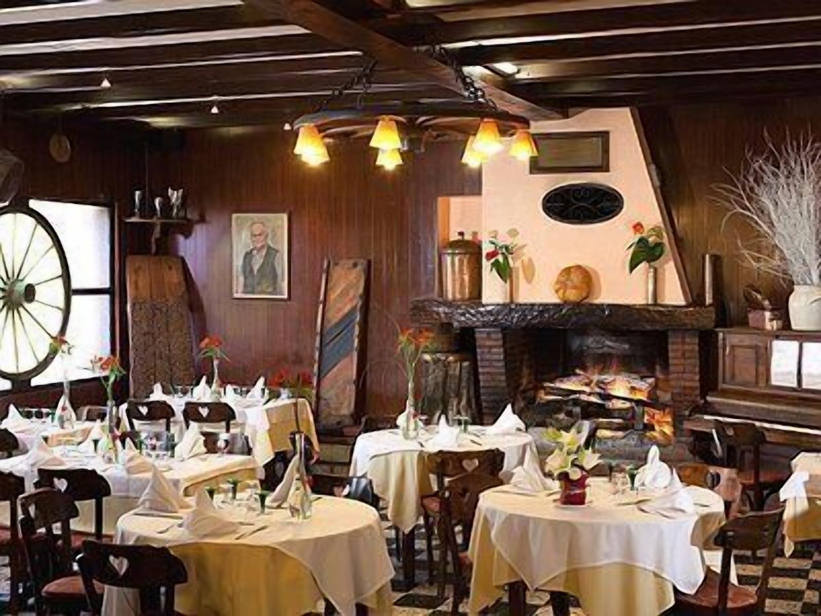 A restaurant with round tables covered in white tablecloths, a wooden ceiling, and a fireplace.