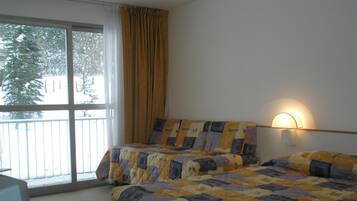 Un dormitorio con dos camas, una ventana con cortinas y una lámpara de pared.