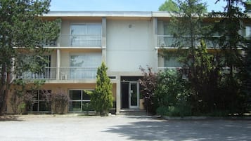 Un edificio de varios pisos con una entrada central, balcones en cada planta y vegetación circundante.