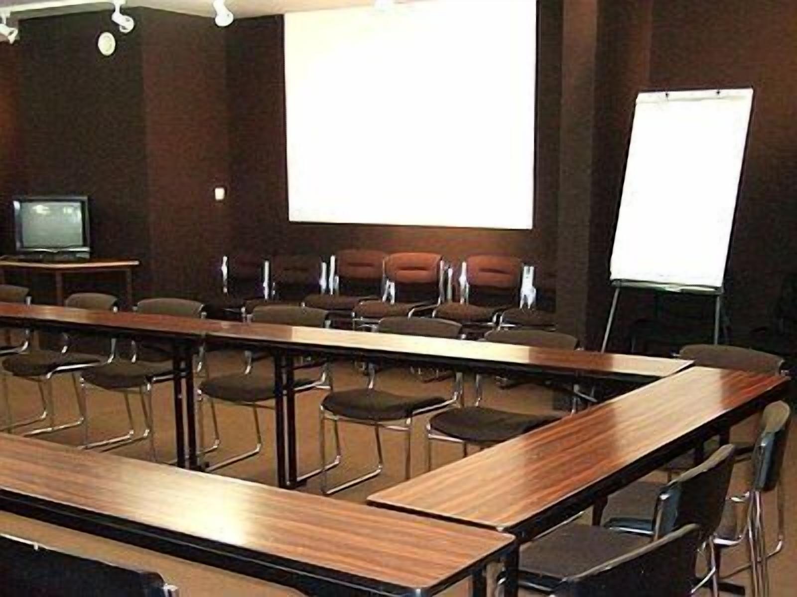Kokoushuone, jossa on pitkä pöytä, useita rivissä olevia tuoleja, projektorikangas ja valkotaulu.