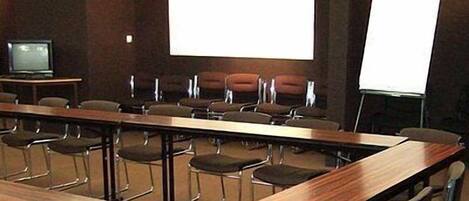 A conference room with a long table, rows of chairs, a projector screen, and a whiteboard.