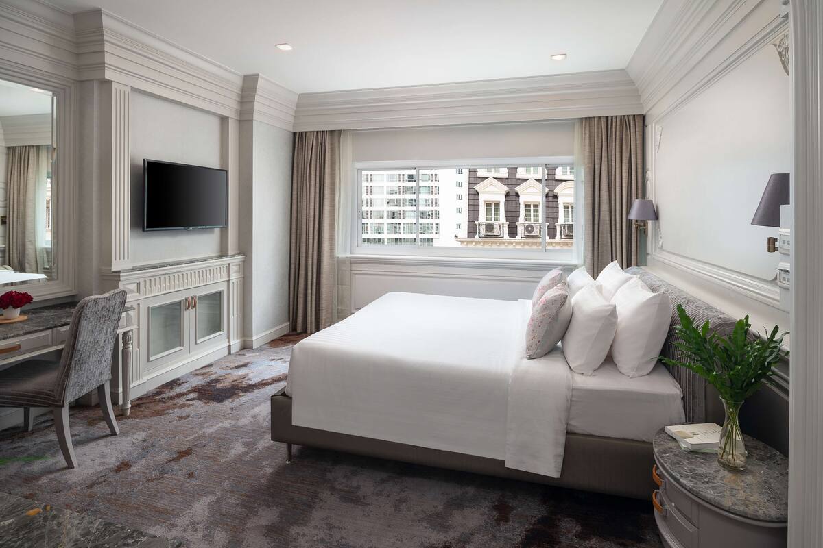 Une chambre d’hôtel avec un grand lit, un téléviseur fixé au mur, un bureau avec une chaise et une fenêtre donnant sur la ville.